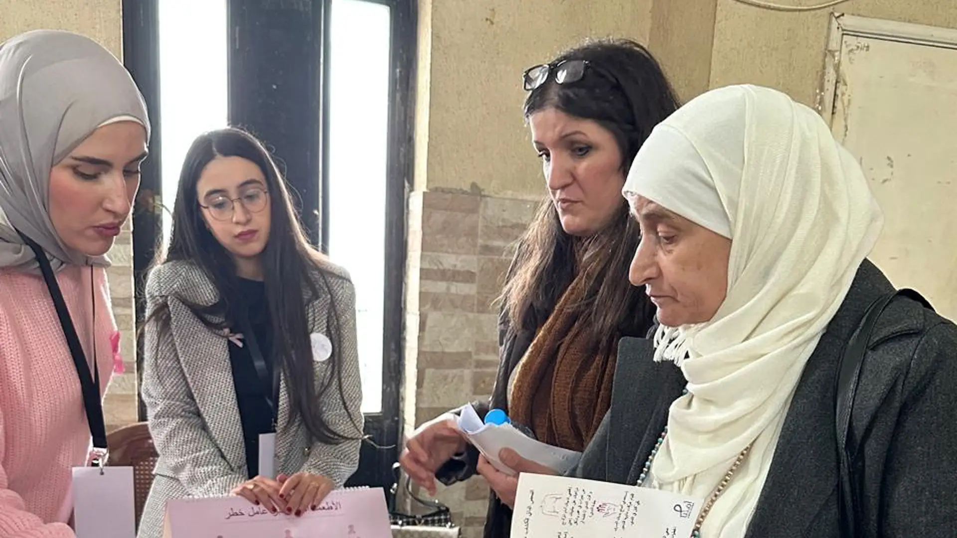 A group of four women - Syrian and Lebanese - in a hall. One of the women is showing something to the others