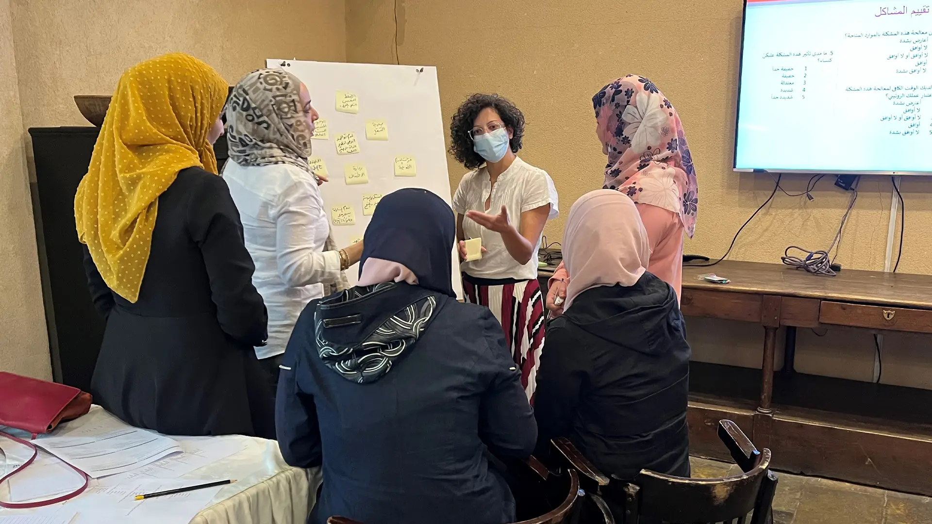 Photo of Muslim women looking at a flipchart. One person is standing by the board speaking. The others have their backs to the viewer